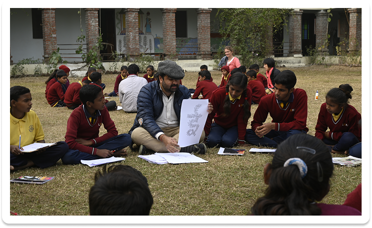 Educator presenting an Akshar Chitra drawing to school children outdoors