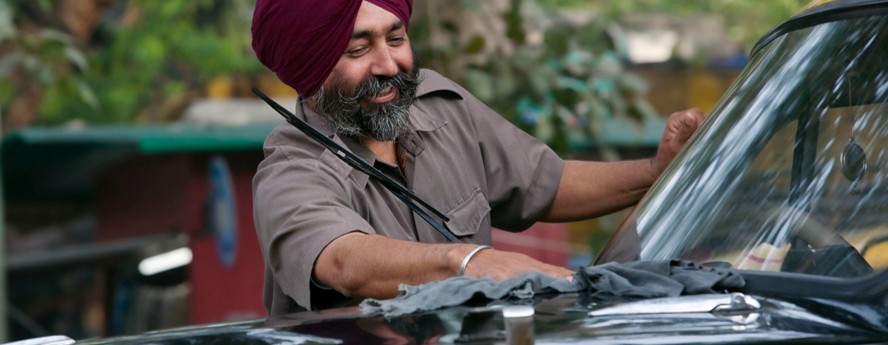 Smiling attendant cleaning a classic black taxi windshield